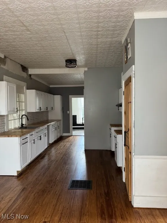 Kitchen featuring white cabinets, butcher block counters, dark wood-style flooring, backsplash, and an ornate ceiling