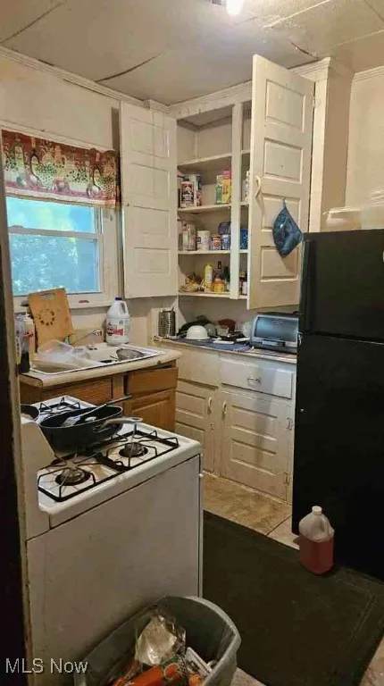 Kitchen featuring white gas range oven, freestanding refrigerator, light countertops, brown cabinetry, and white cabinetry