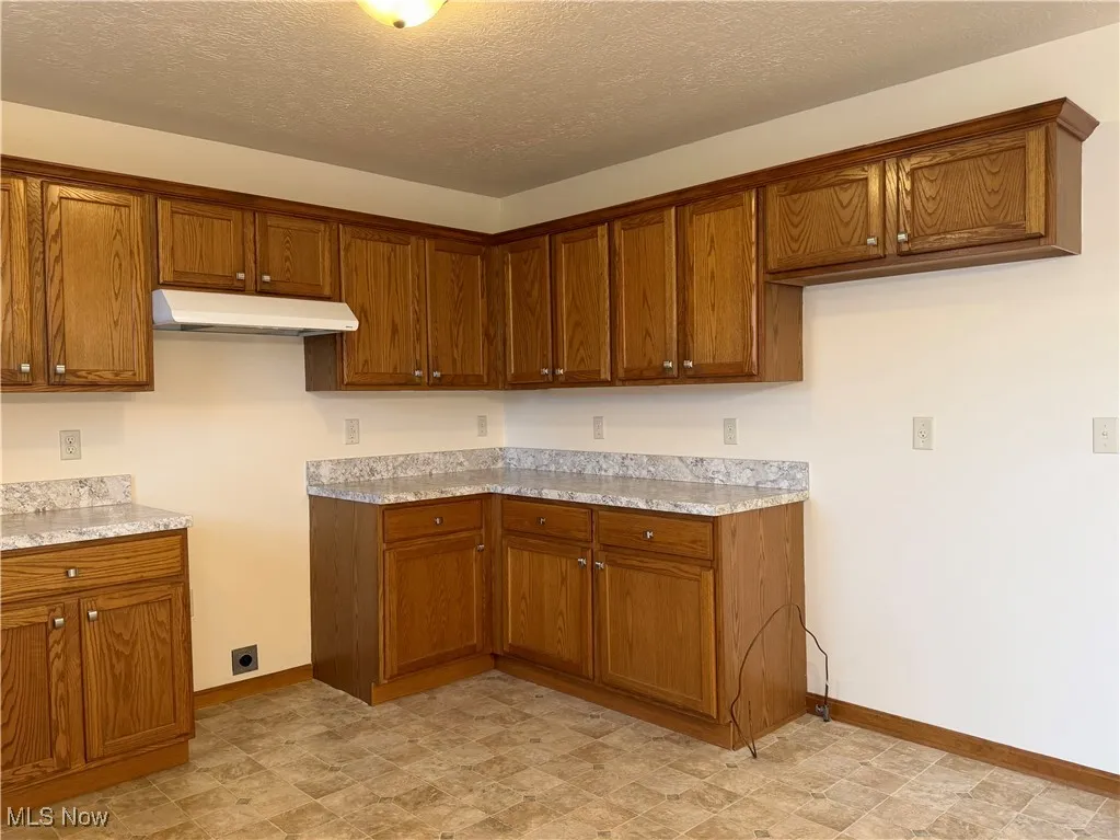 Kitchen with brown cabinetry, a textured ceiling, and under cabinet range hood