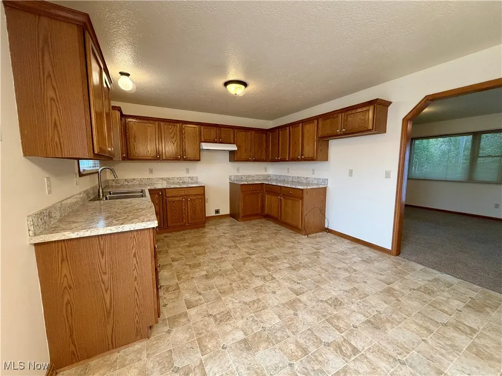 Kitchen featuring brown cabinets, light countertops, a textured ceiling, and under cabinet range hood