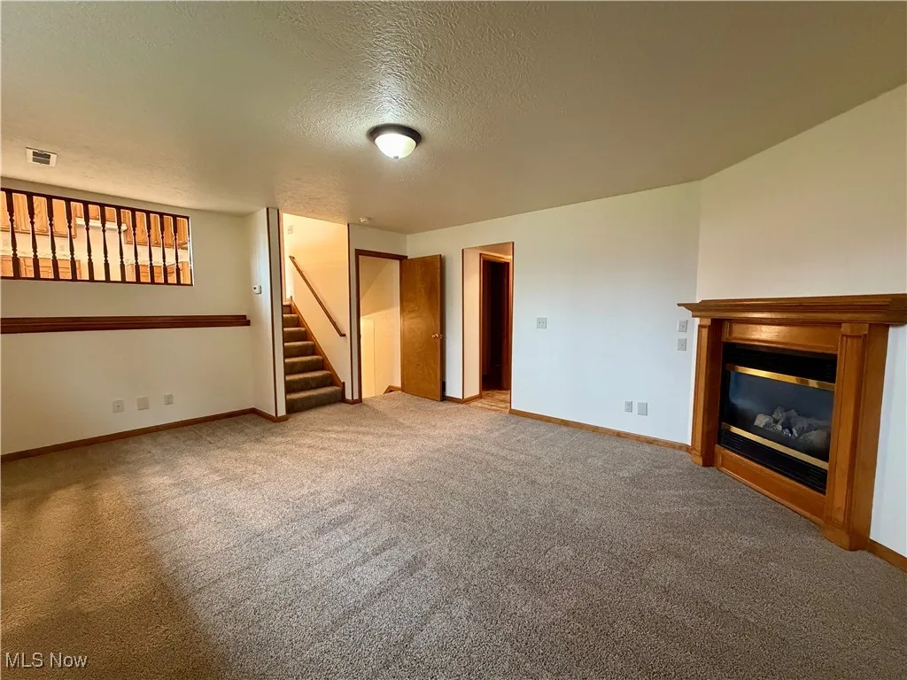 Unfurnished living room featuring a textured ceiling, light colored carpet, and stairway