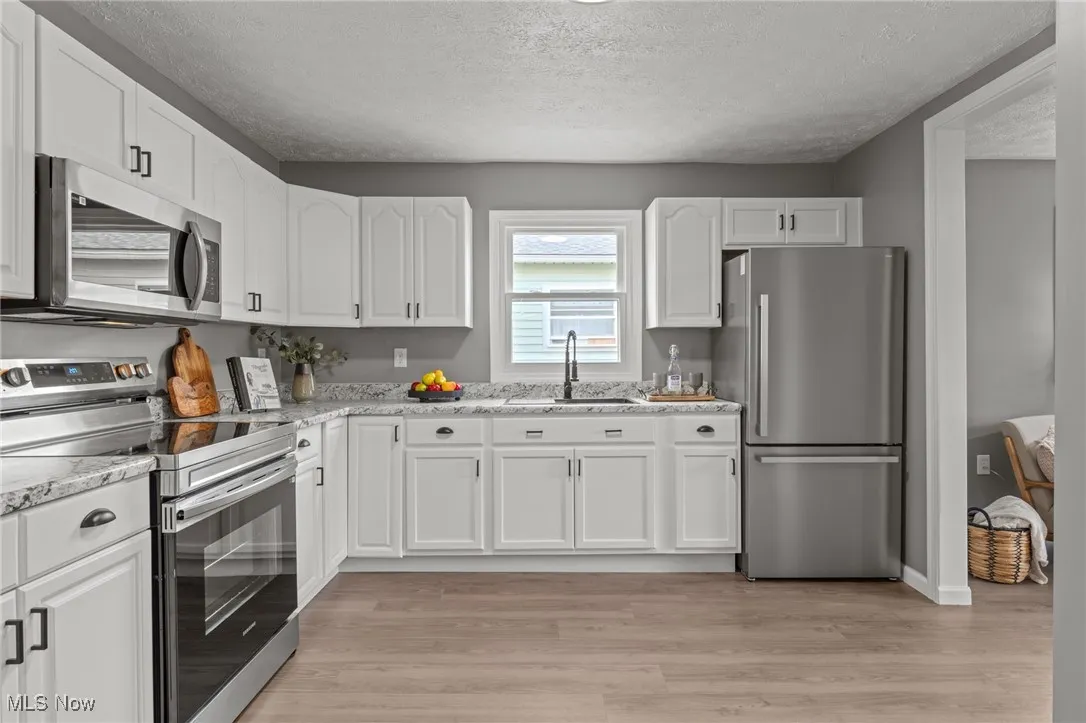 Kitchen with stainless steel appliances, white cabinetry, a textured ceiling, light wood-type flooring, and light stone countertops
