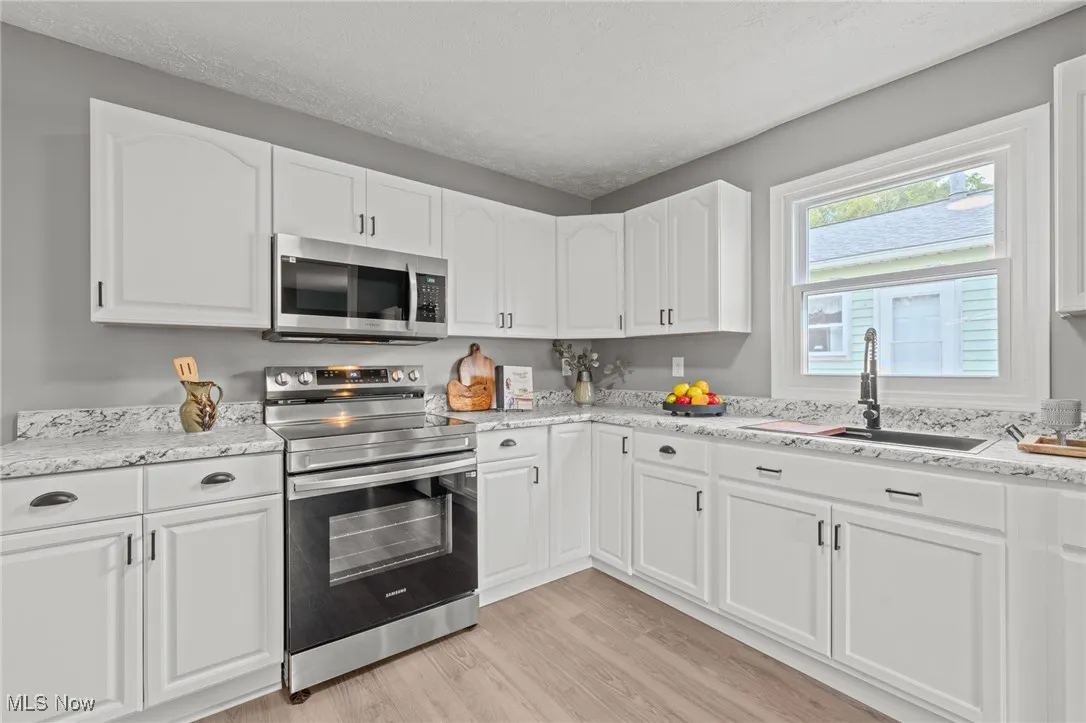 Kitchen featuring appliances with stainless steel finishes, white cabinetry, light wood finished floors, and a textured ceiling