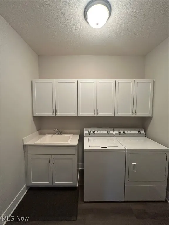 Washroom with a textured ceiling, washer and dryer, cabinet space, and dark wood-style flooring