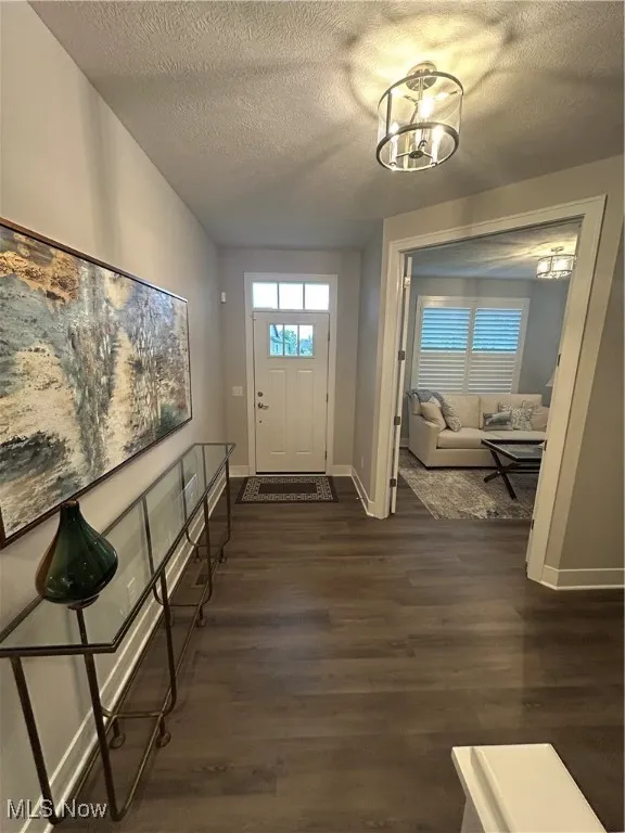 Entryway with dark wood-style flooring, a textured ceiling, and a chandelier