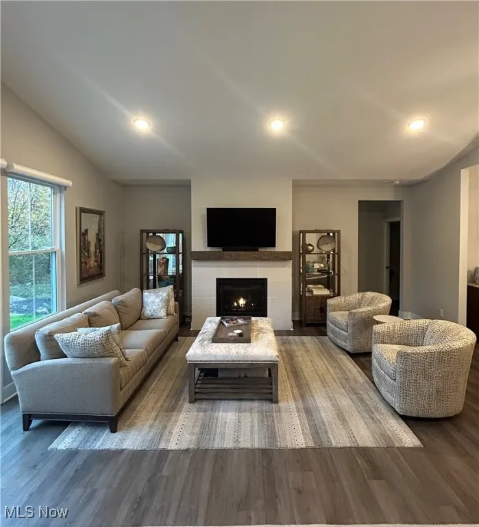 Living room with wood finished floors, a tiled fireplace, and recessed lighting