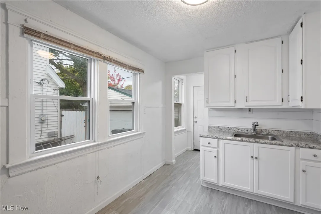 Kitchen featuring white cabinets, a textured ceiling, light wood finished floors, and light stone countertops