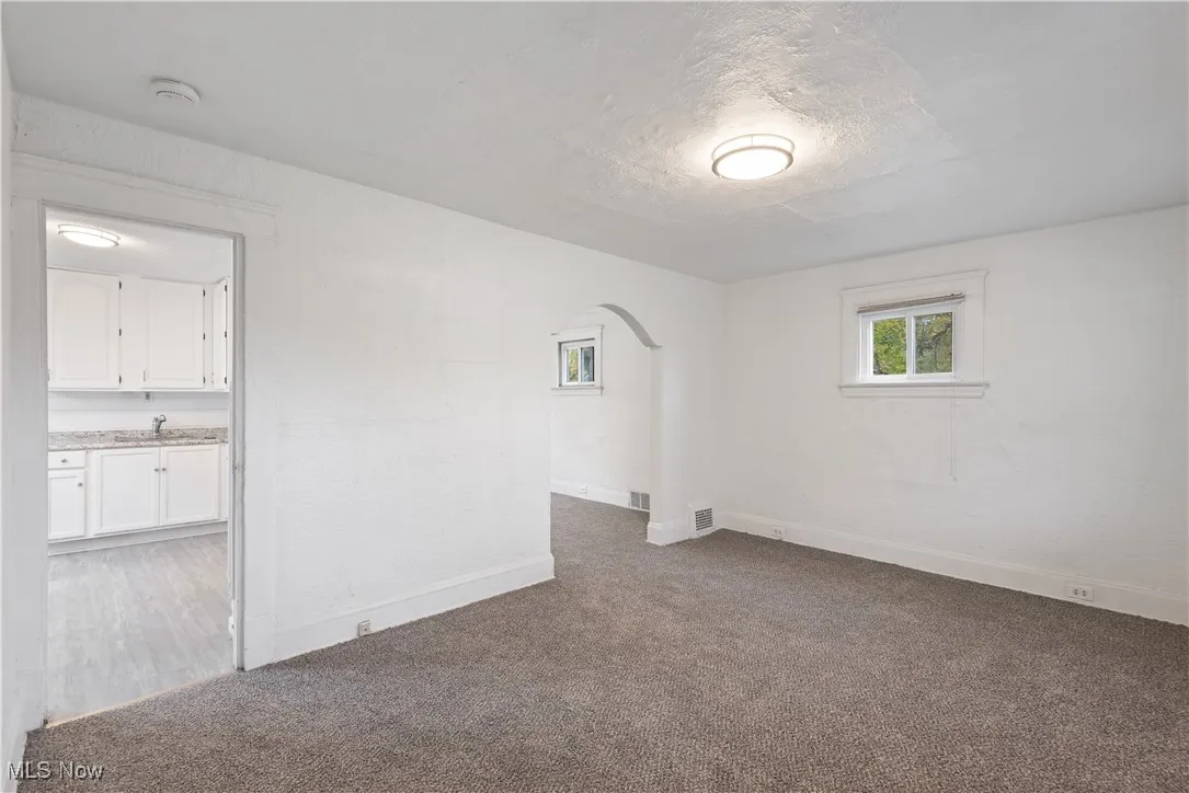 Unfurnished room featuring arched walkways, dark carpet, and a textured ceiling