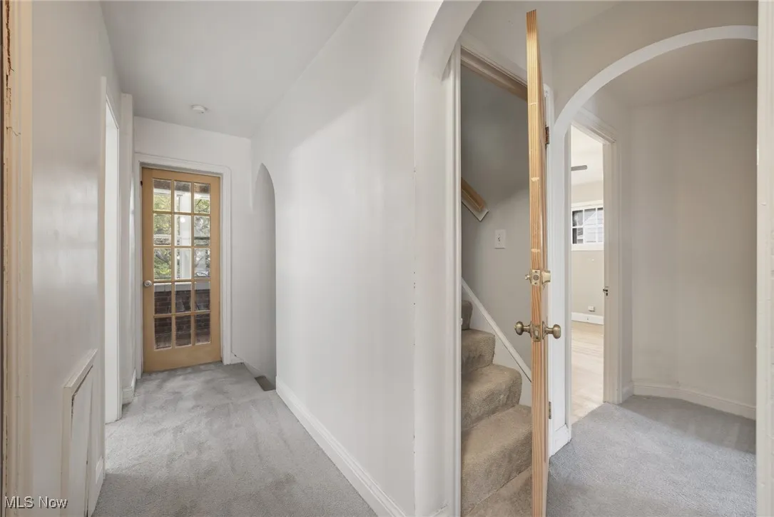Corridor with arched walkways, light colored carpet, and stairway