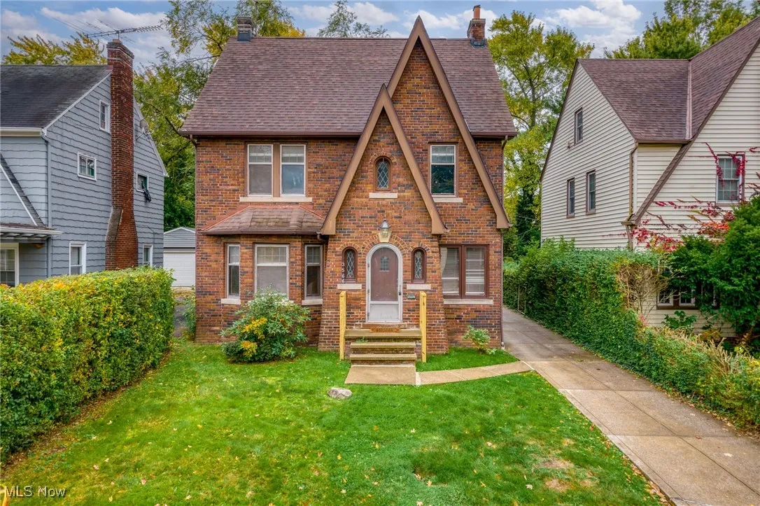 Tudor house with brick siding, a front yard, a shingled roof, and a chimney