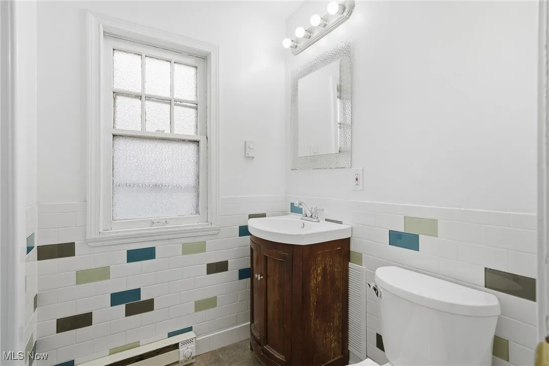 Half bathroom with tile walls, vanity, wainscoting, and a baseboard heating unit