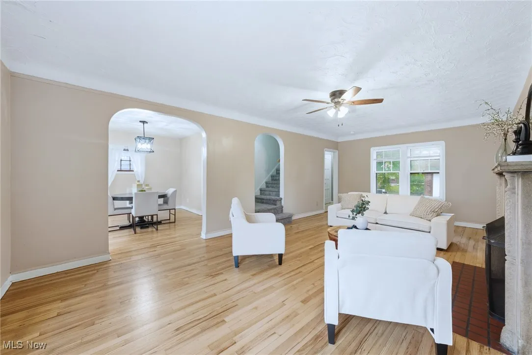 Living area featuring arched walkways, light wood-style flooring, ceiling fan, stairs, and a chandelier