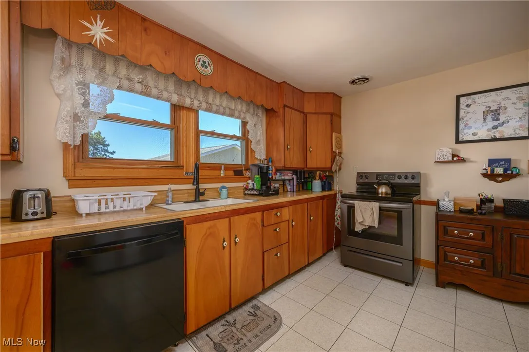 Kitchen with electric range, dishwasher, light countertops, brown cabinets, and light tile patterned floors