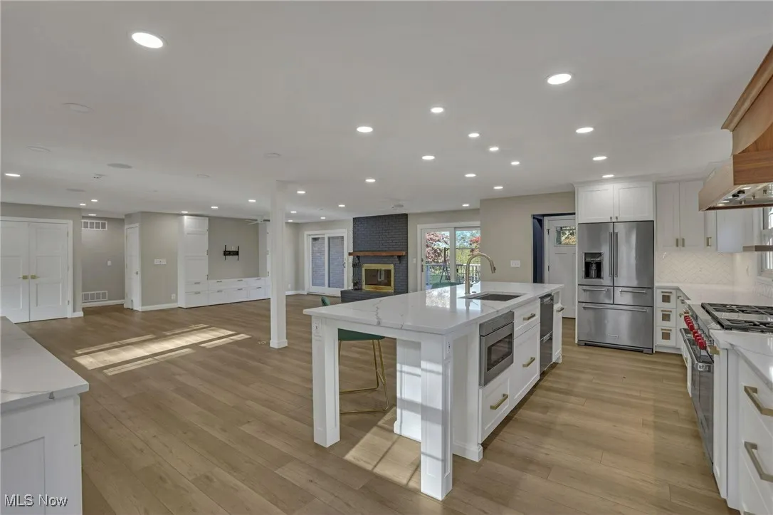 Kitchen featuring open floor plan, white cabinetry, premium appliances, light stone countertops, and tasteful backsplash