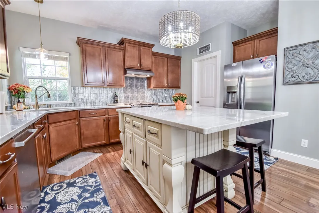 Kitchen with a kitchen bar, decorative backsplash, light wood-style flooring, light stone counters, and appliances with stainless steel finishes