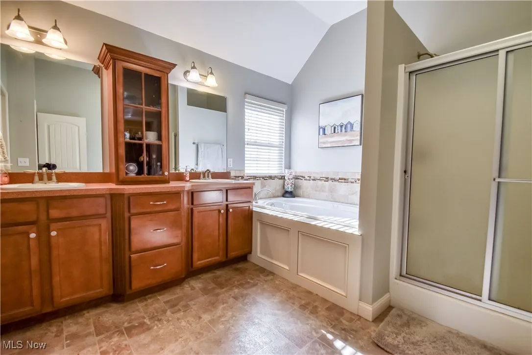 Full bathroom with double vanity, a garden tub, vaulted ceiling, and a shower stall