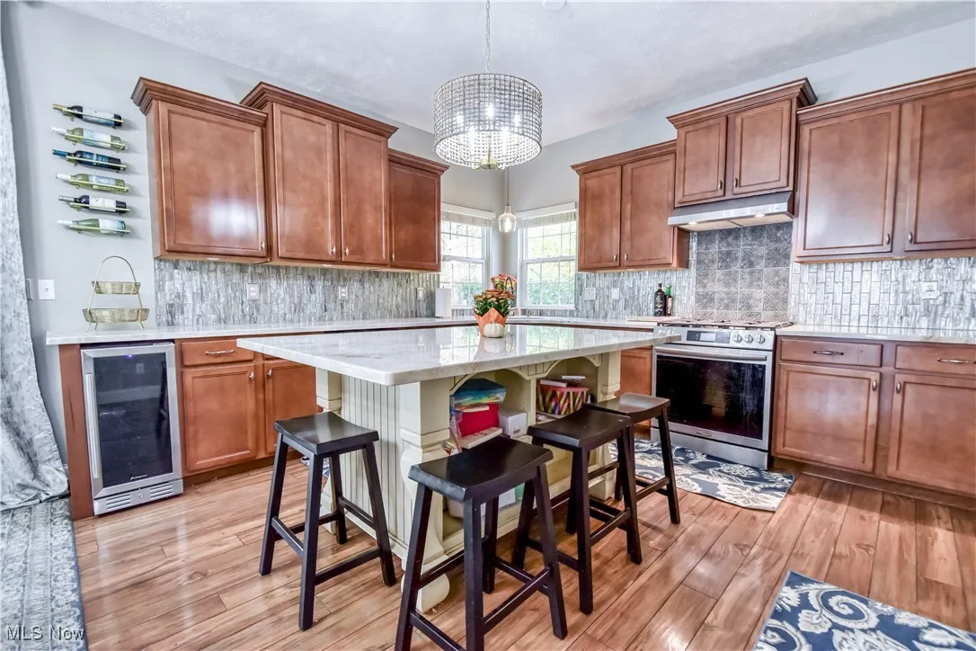 Kitchen with stainless steel range oven, brown cabinets, wine cooler, pendant lighting, and a kitchen breakfast bar