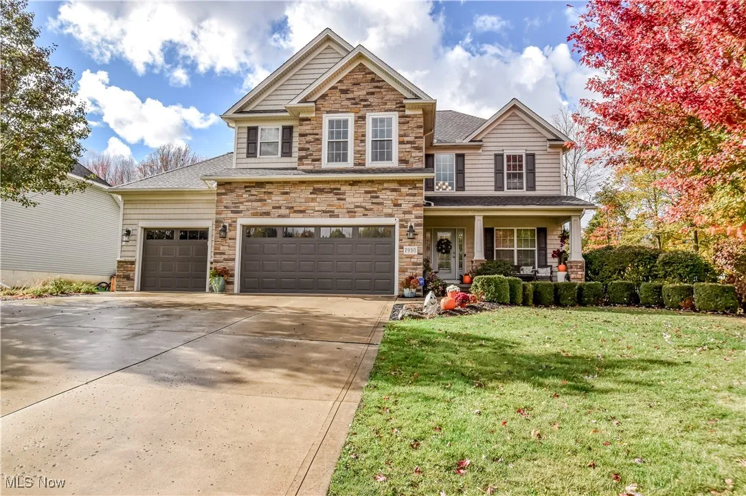 View of front of property featuring stone siding, concrete driveway, covered porch, a front lawn, and a garage