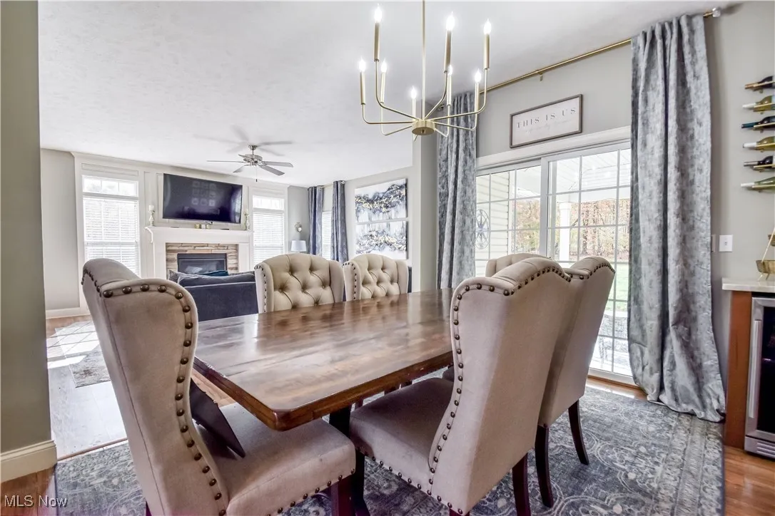 Dining room featuring dark wood-style flooring, a stone fireplace, a chandelier, ceiling fan, and wine cooler