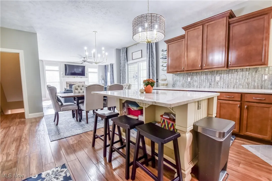 Kitchen with brown cabinets, a breakfast bar area, backsplash, pendant lighting, and light stone countertops