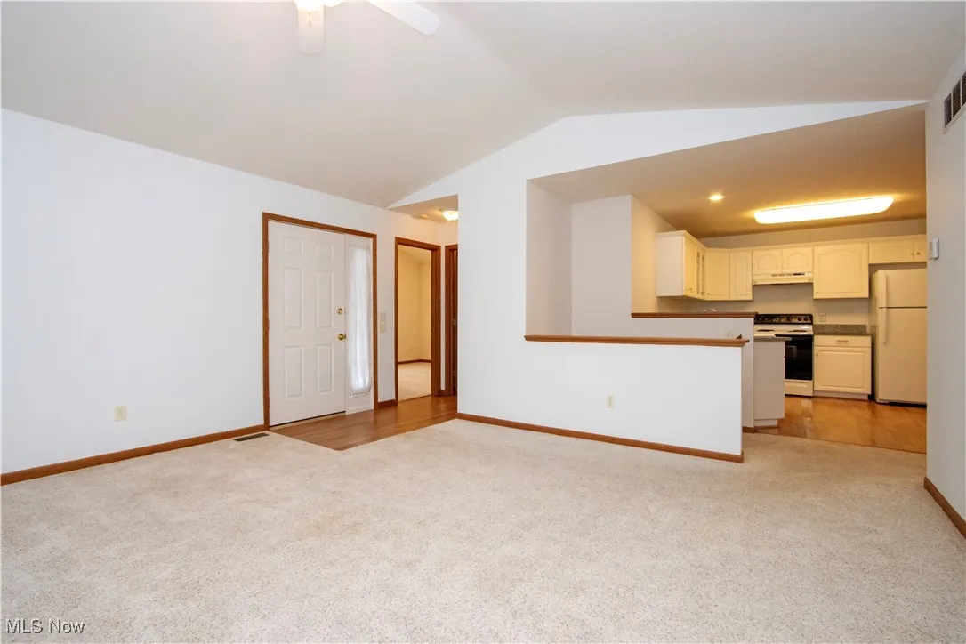 Unfurnished living room with light carpet, vaulted ceiling, and a ceiling fan