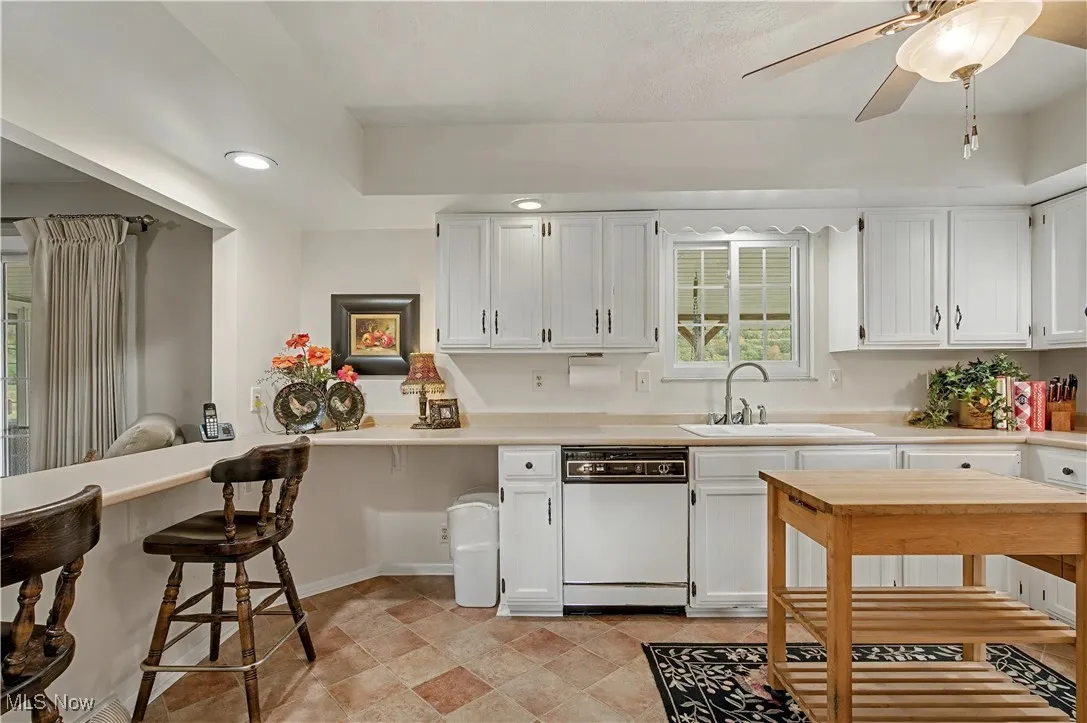 Kitchen with light countertops, white cabinetry, dishwasher, a breakfast bar, and ceiling fan