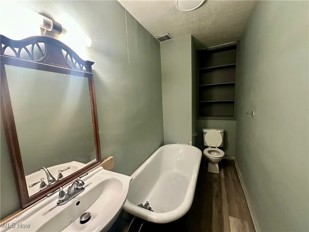Bathroom featuring a soaking tub, a textured ceiling, wood finished floors, and built in shelves