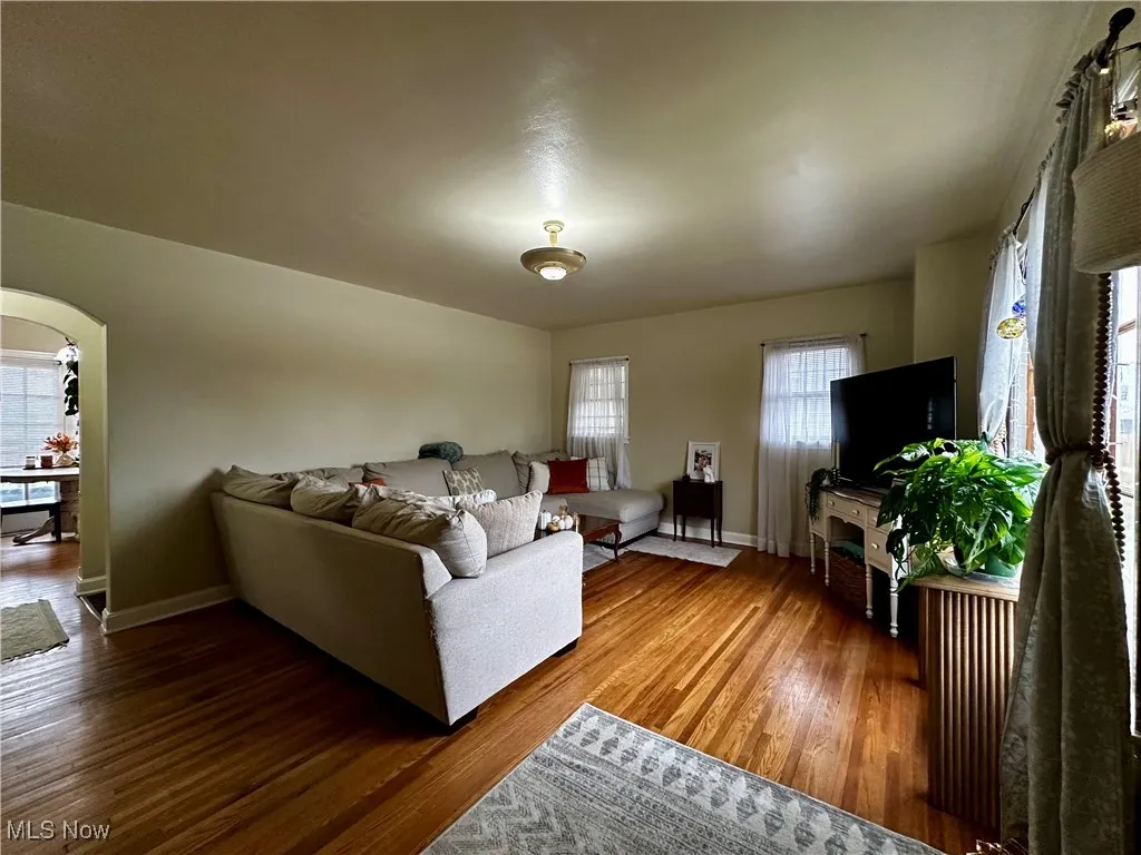 The large living room features original hardwood flooring and an arched entry leading to the dining room.