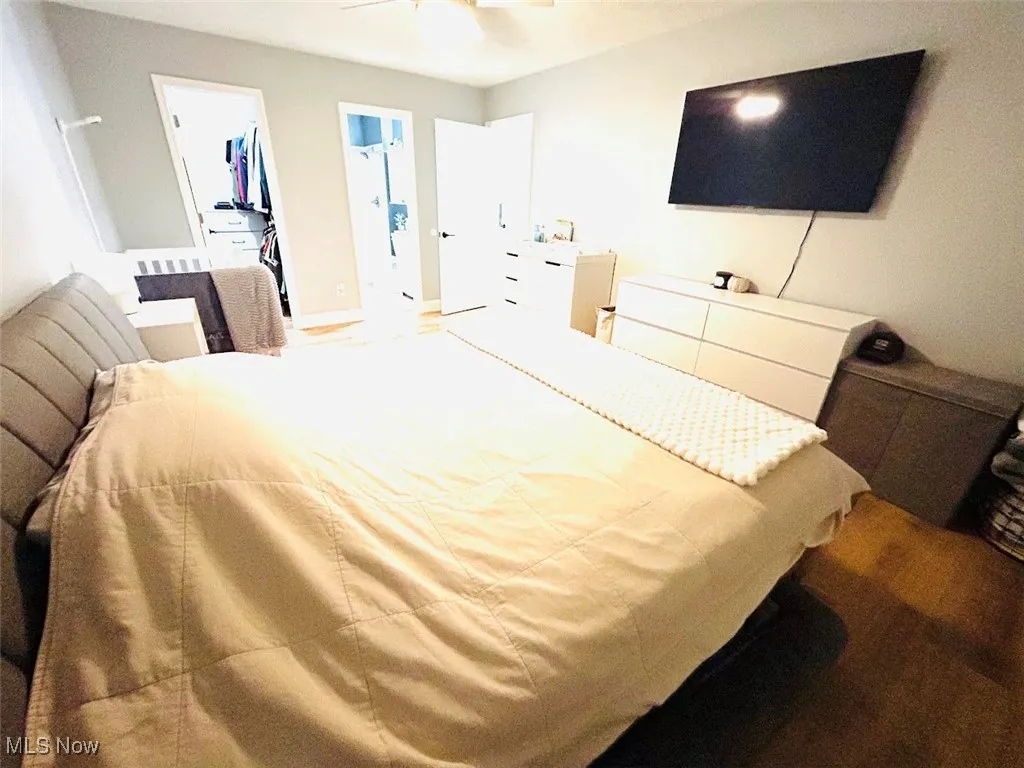 Bedroom featuring wood finished floors, a spacious closet, connected bathroom, and a ceiling fan