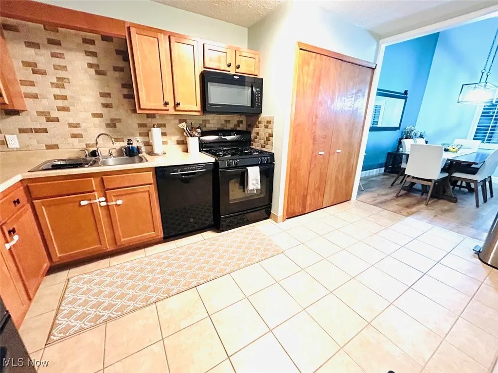 Kitchen with black appliances, decorative backsplash, light countertops, light tile patterned floors, and a textured ceiling