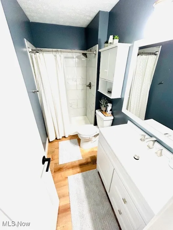 Full bath with curtained shower, a textured ceiling, vanity, and light wood finished floors