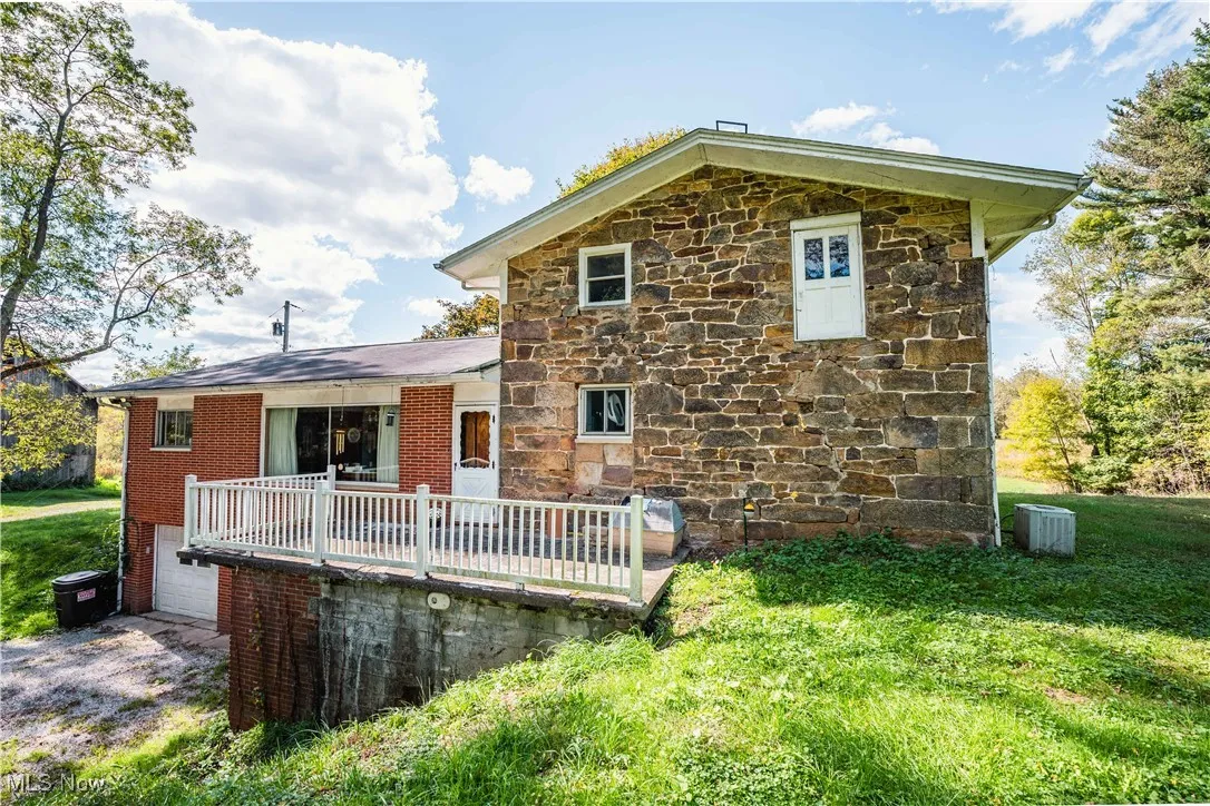 Rear view of house featuring a wooden deck, stone siding, a garage, driveway, and a lawn