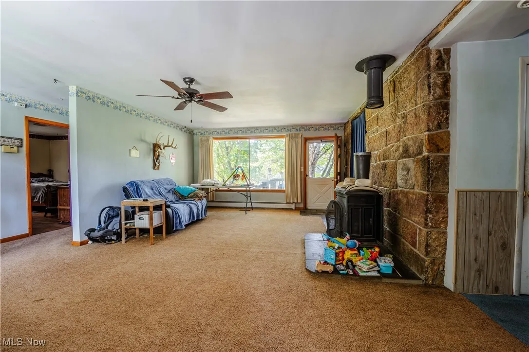 Living area with a wood stove, carpet flooring, baseboard heating, and a ceiling fan