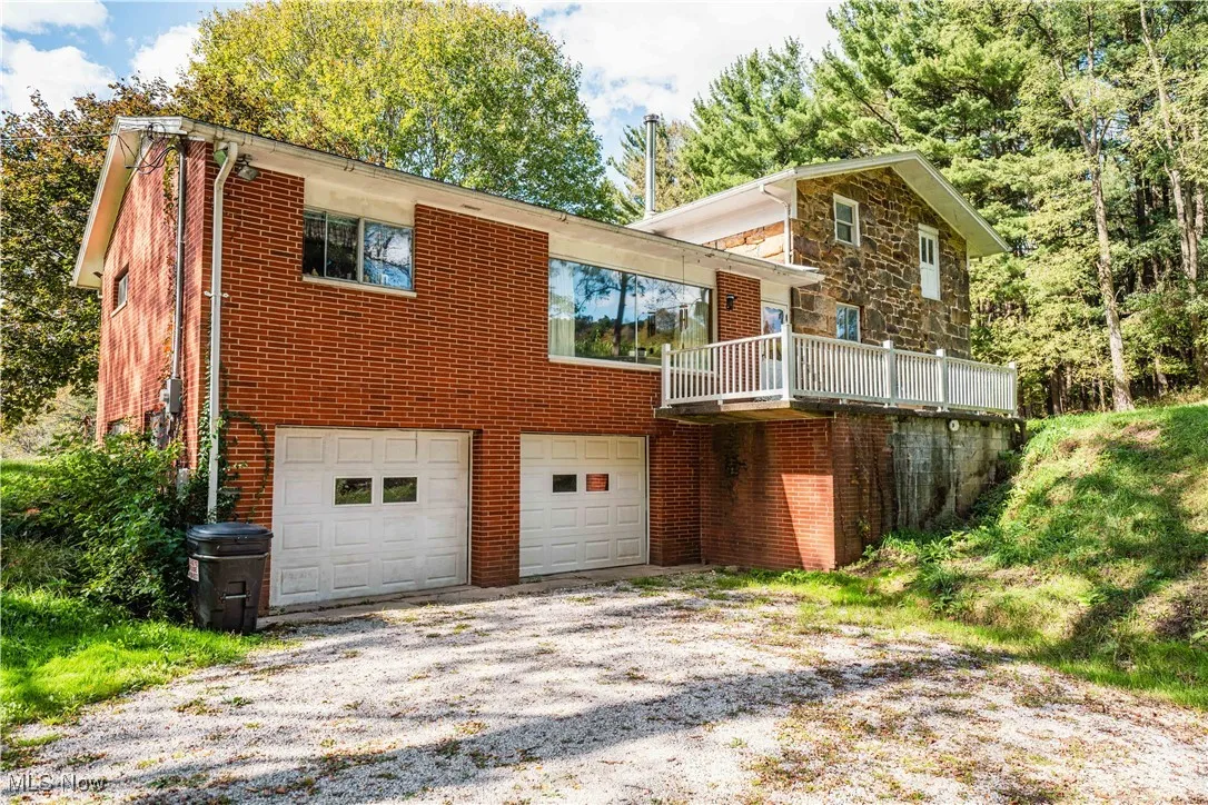 Back of house with a garage, brick siding, driveway, and a balcony