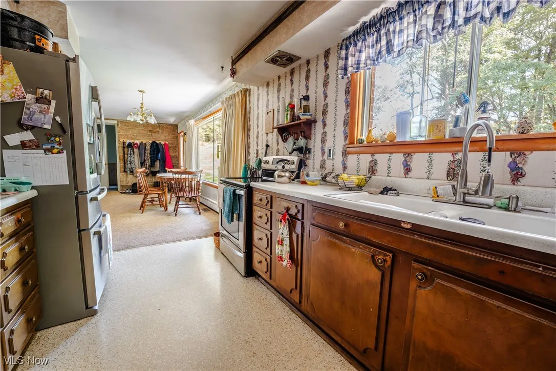 Kitchen featuring stainless steel appliances, light countertops, open shelves, a chandelier, and hanging light fixtures
