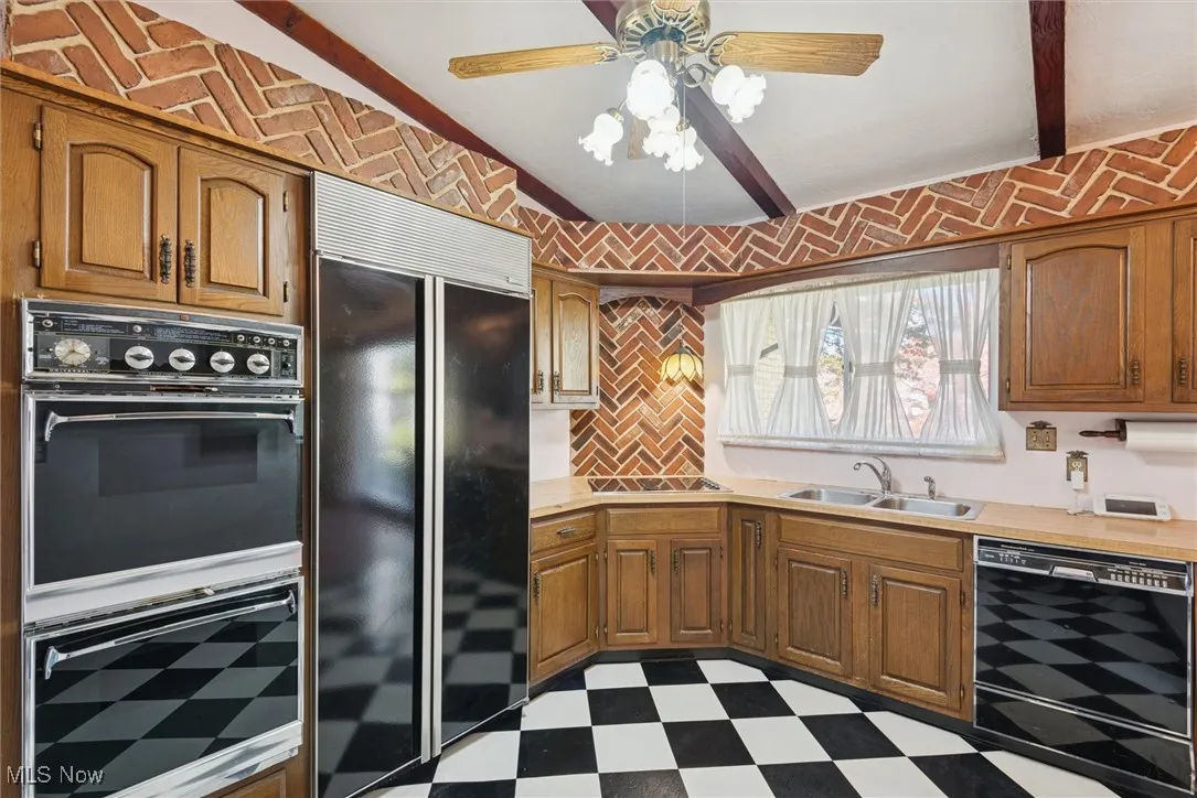 Kitchen featuring dark floors, light countertops, black appliances, and brown cabinetry