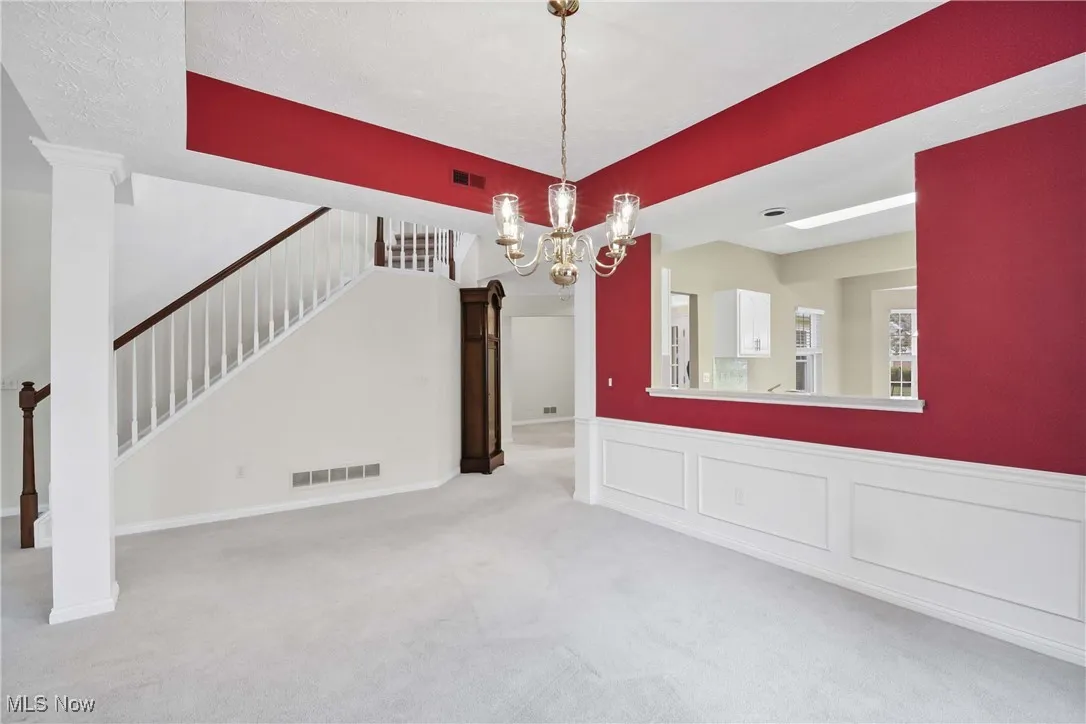 Unfurnished dining area featuring carpet floors, a chandelier, stairway, a decorative wall, and wainscoting