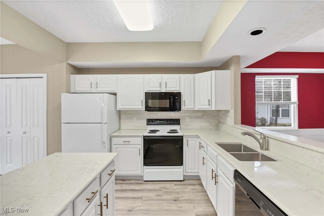 Kitchen with black appliances, light stone countertops, backsplash, white cabinetry, and a textured ceiling
