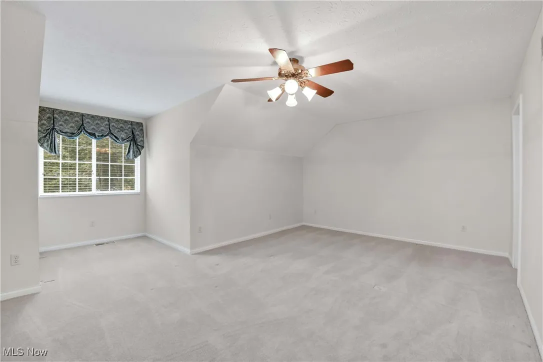 Additional living space featuring light carpet, vaulted ceiling, a ceiling fan, and a textured ceiling