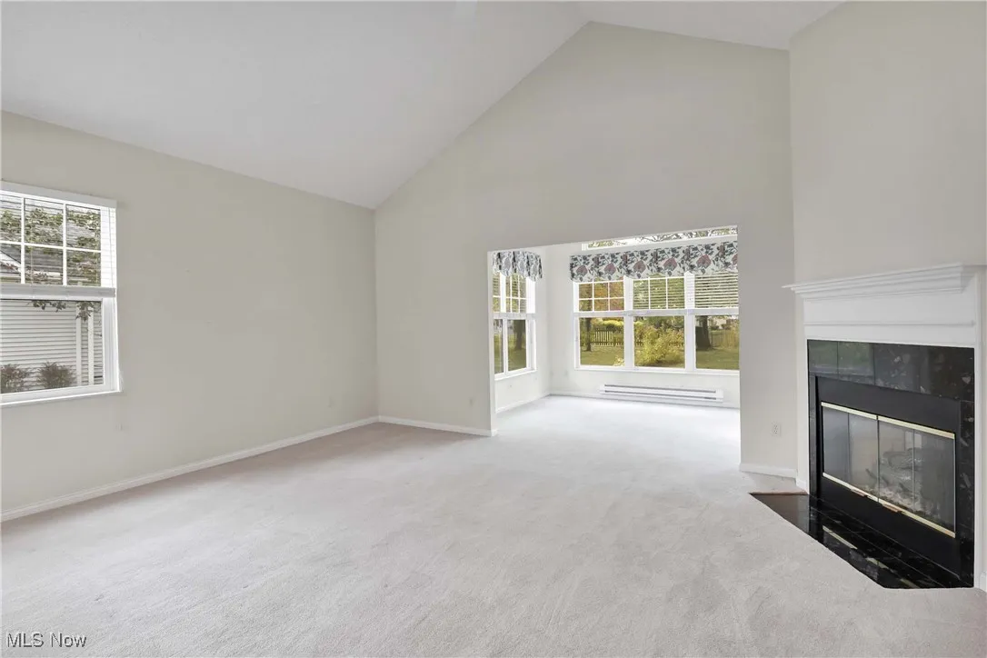 Unfurnished living room with high vaulted ceiling, light carpet, a tiled fireplace, and baseboard heating