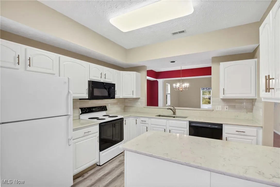 Kitchen featuring black appliances, white cabinetry, a textured ceiling, tasteful backsplash, and a chandelier