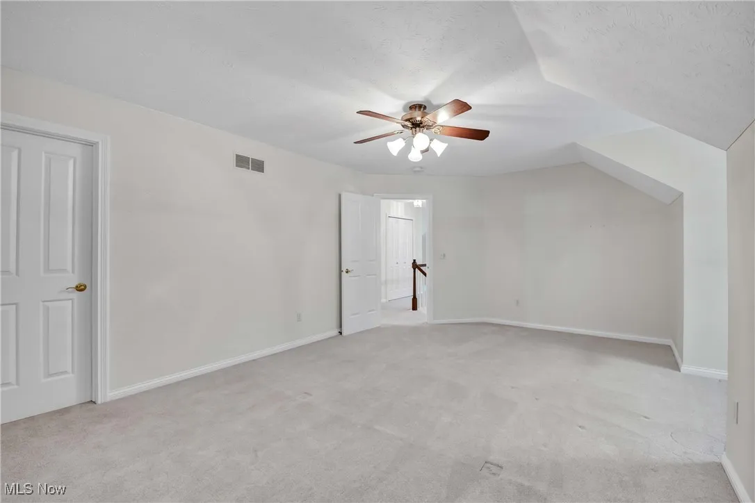 Additional living space with light carpet, a textured ceiling, and ceiling fan