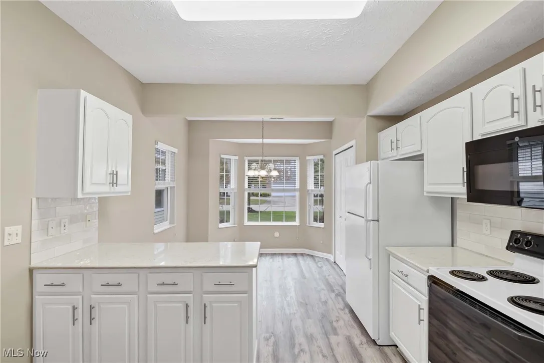 Kitchen featuring backsplash, white electric stove, black microwave, white cabinetry, and light stone countertops