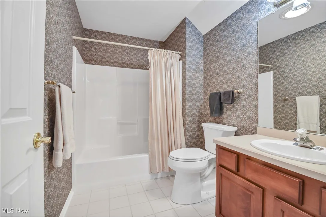 Bathroom with light tile patterned floors, vanity, shower / bath combo with shower curtain, and wallpapered walls