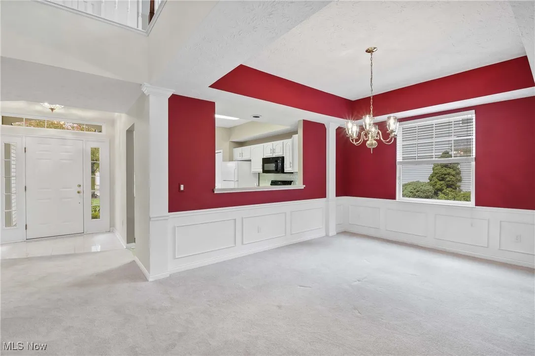 Unfurnished dining area featuring carpet, a decorative wall, wainscoting, a textured ceiling, and a chandelier