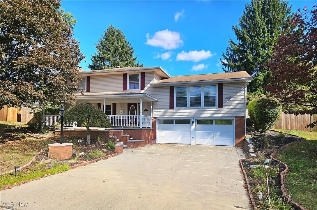 Split level home featuring driveway, a porch, a garage, and brick siding