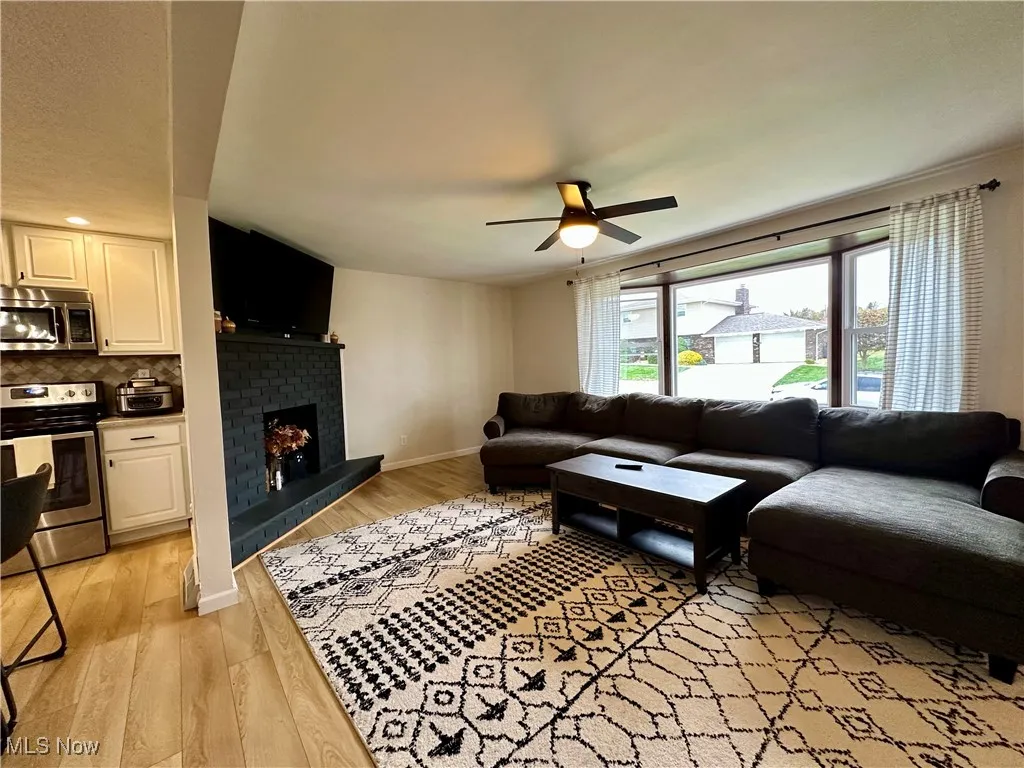Living area featuring light wood-style flooring, a brick fireplace, and ceiling fan