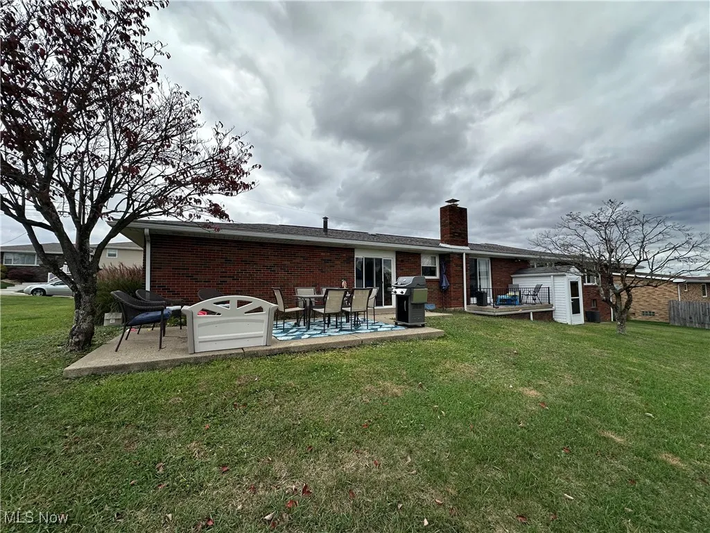 Back of house featuring brick siding, a yard, a chimney, and a patio area