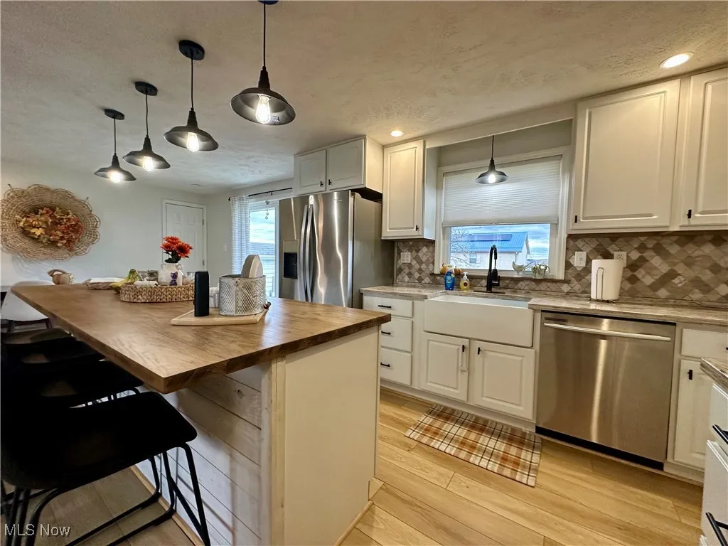 Kitchen featuring decorative light fixtures, appliances with stainless steel finishes, a breakfast bar, a textured ceiling, and tasteful backsplash