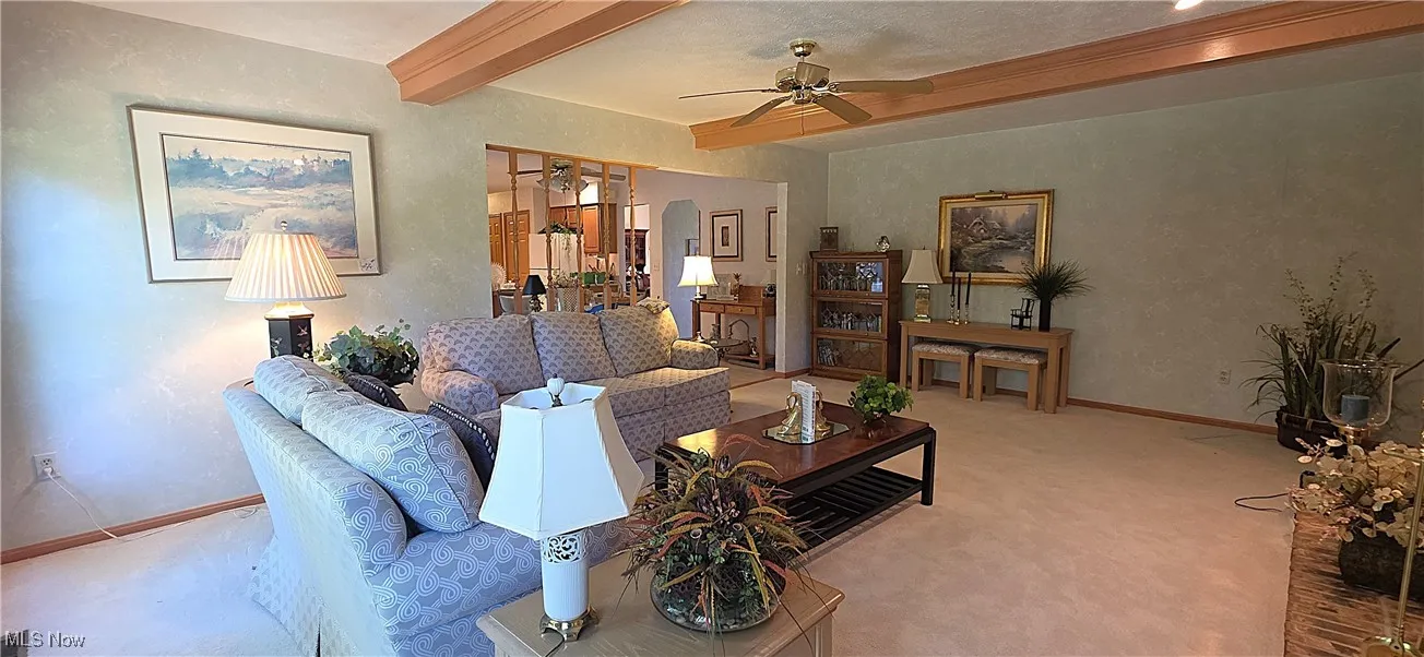 Family room featuring a beamed ceiling, a fireplace, and a ceiling fan